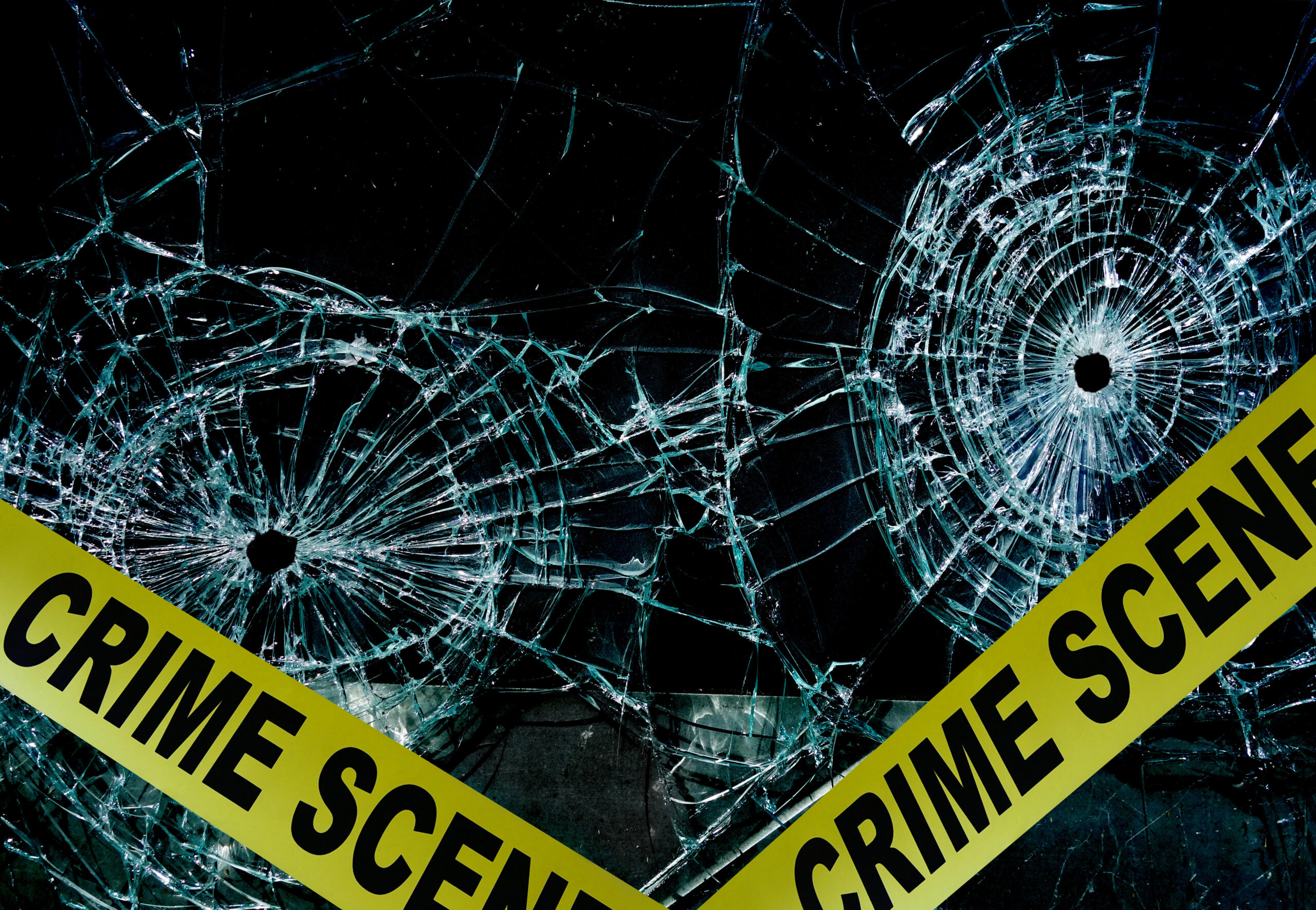 Police tape across broken glass with bullet holes