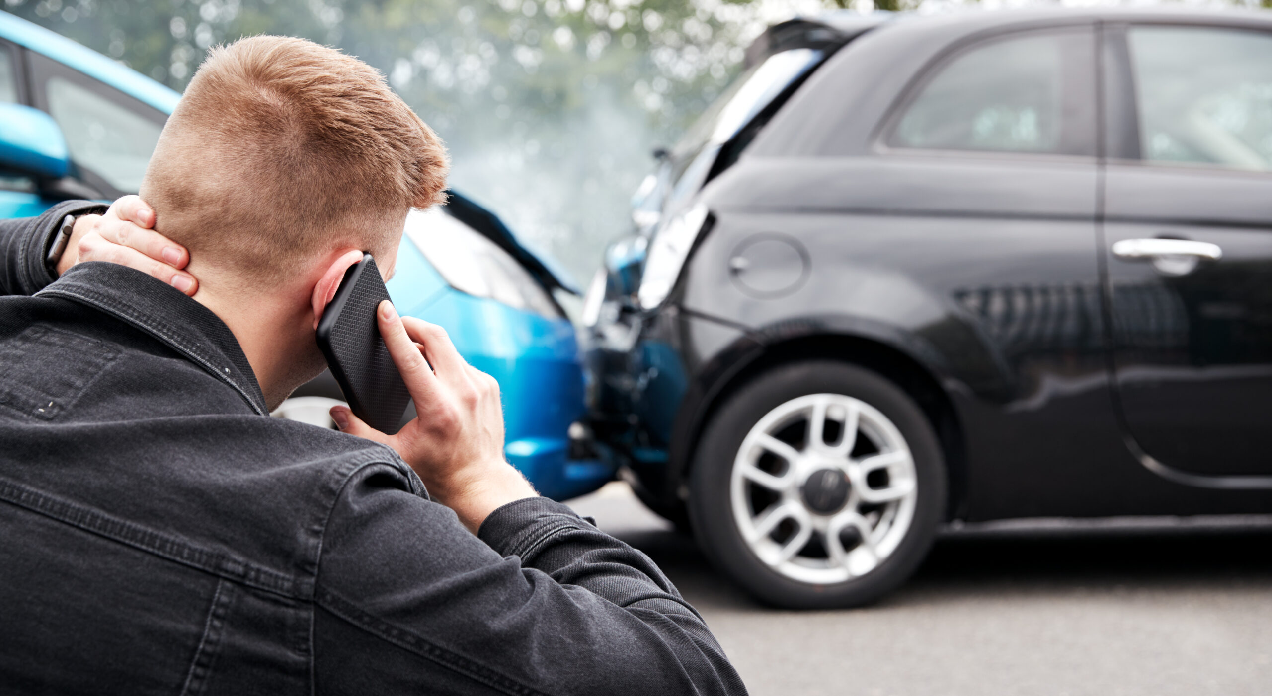 Image of a man on the phone after a car accident. He is rubbing his neck indicating whiplash or a neck injury.