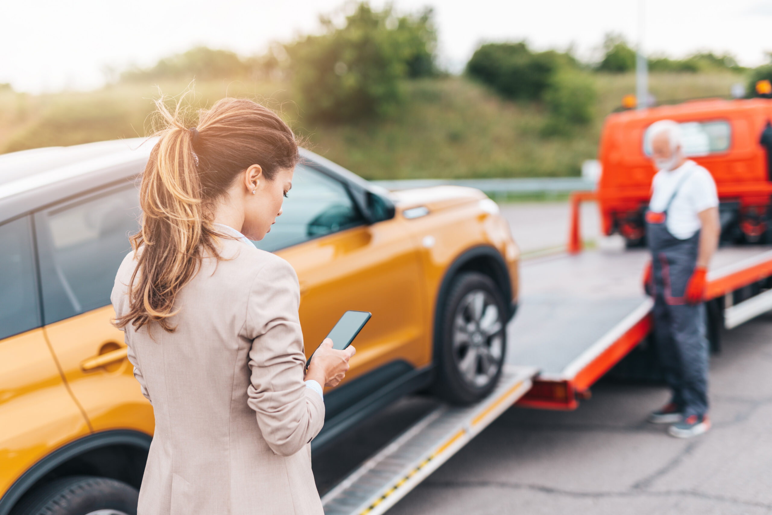 Woman searching for a truck accident lawyer on her phone as her car is towed away after an accident